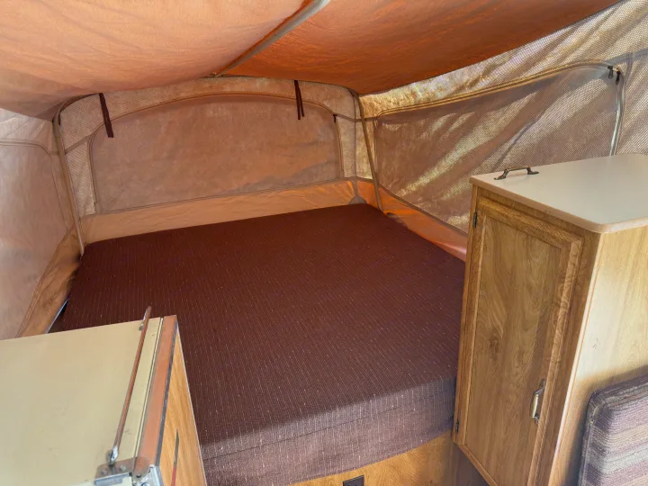 RV rental interior showing a pop-up camper bed, mesh windows, and wooden cabinetry.. Coleman Grand Tour Shenandoah 1987