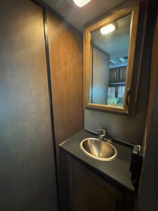 Compact RV rental bathroom featuring a sink, mirror, and dark countertop with wooden cabinetry.. Thor Majestic 2018