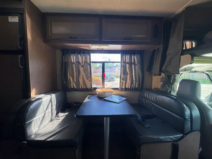 Interior of an **rv rental** showing the dinette area with a table, two black leatherette benches, and a sunny window view.. Thor Majestic 2018