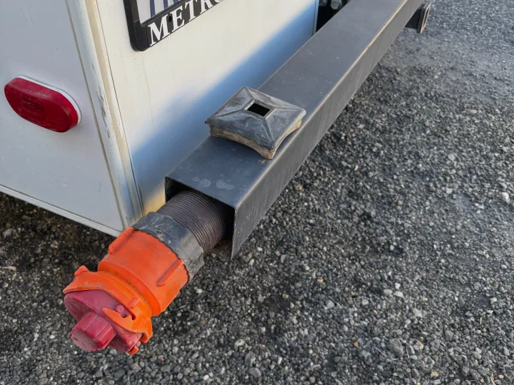 RV rental's rear: CA plate 7NIZ554, a hollow bumper with an orange shore power plug, on gravel.. Forester LE 2016