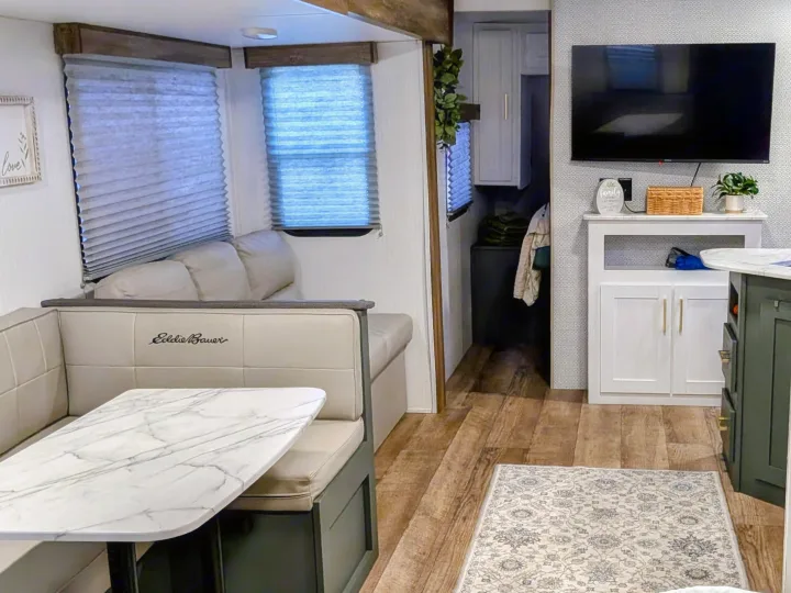 Inside a modern RV rental: a light-toned dinette with marble table, pleated window blinds, wood flooring, and a TV living area.. Eddie Bauer Eddie Bauer 2024