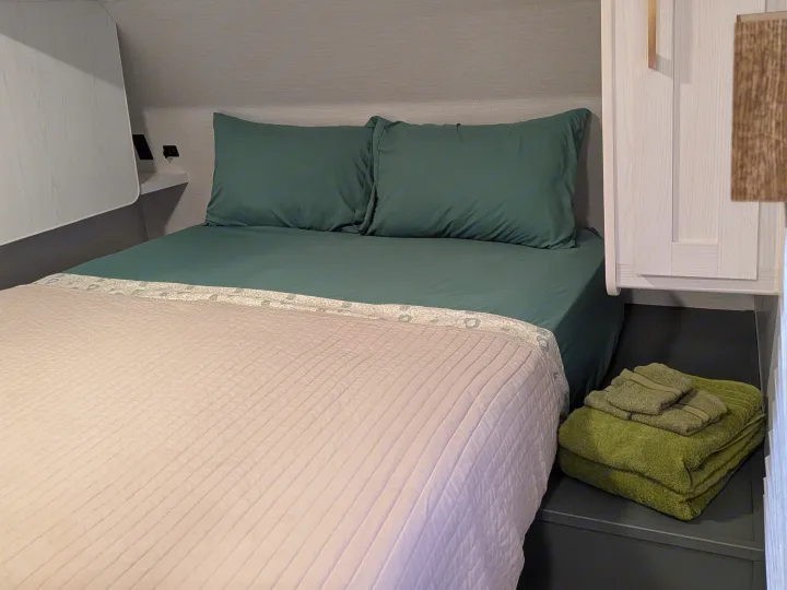 Comfortable RV rental bedroom featuring dark green bedding, a light quilted comforter, and green towels. Ideal for travel.. Eddie Bauer Eddie Bauer 2024