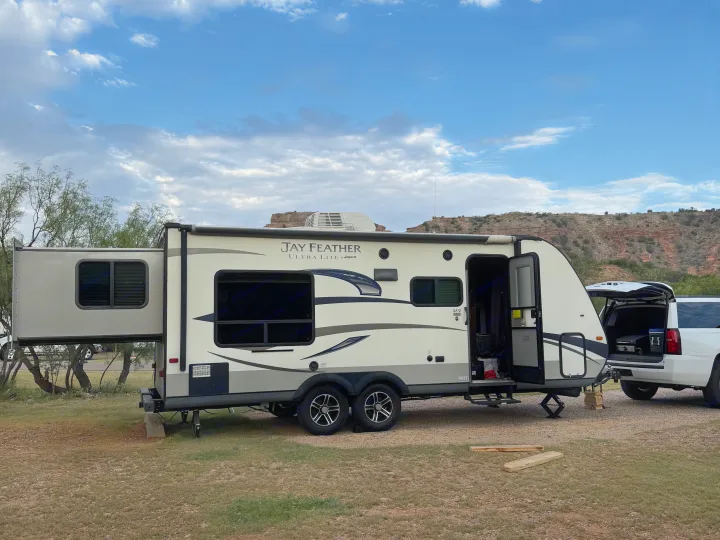 This Jay Feather RV rental is set up with its slide-out extended for a scenic outdoor camping adventure with mountains behind.. Jayco Jay Feather Ultra Lite 2015