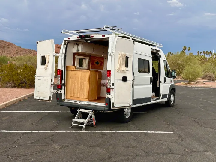 Custom white camper van, doors open to reveal its built-in interior. Parked in a desert. Consider this RV rental for your next trip!. RAM Promaster 2018