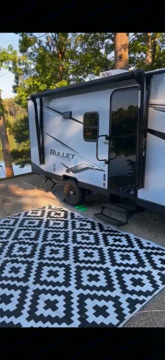 Scenic rv rental at a lakeside campsite with a black & white outdoor rug. Perfect for your next outdoor adventure.. Keystone RV Bullet Crossfire 2024