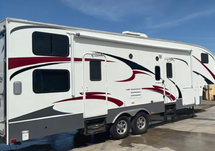 This large white travel trailer RV rental, featuring striking red/black decals, multiple windows, and an extended awning.. Keystone RV Fuzion Toy Hauler 2009