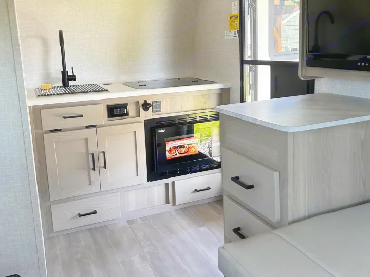 Step inside this compact RV rental's modern kitchen with sink, cooktop, microwave, and ample storage for comfortable travels.. Forest River Rockwood Geo Pro 2023
