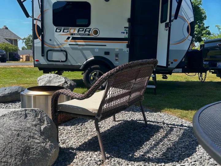 Sunny day at an RV rental: a GEO PRO travel trailer under its awning, with a fire pit & chair on a gravel patio.. Forest River Rockwood Geo Pro 2023