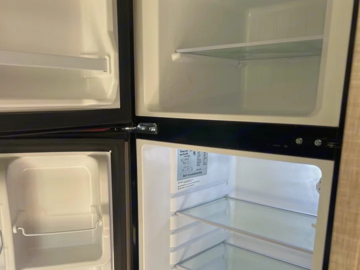 Clean, empty RV rental refrigerator and freezer interior, featuring glass shelves for your travel provisions.. Forest River Rockwood Geo Pro 2023