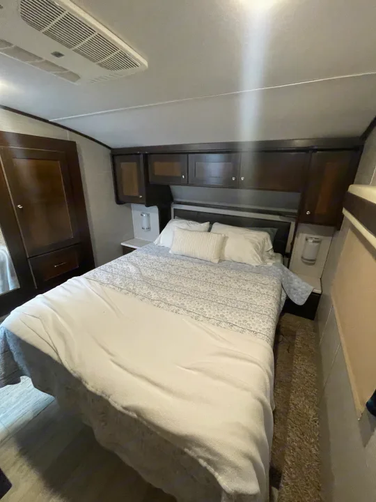 RV rental master bedroom: queen bed, overhead cabinets, side storage, and ceiling AC unit. A compact, functional travel space.. Vanleigh RV Pinecrest 2020