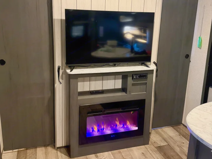 An RV rental's entertainment center with a large TV, glowing electric fireplace, and functional sliding doors.. Dutchmen Aspen Trail LE 26BH 2022