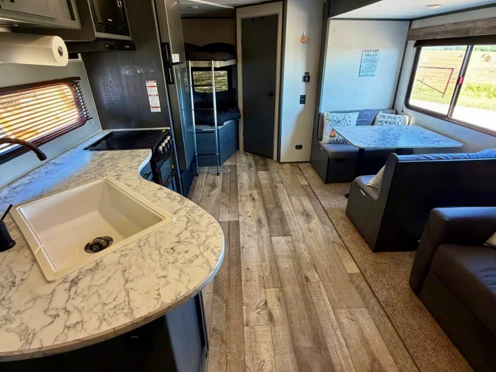 Spacious RV rental interior with kitchen, dining, and living areas. Features include a sink, stove, dinette, sofa, and bunk beds.. Dutchmen Aspen Trail LE 26BH 2022