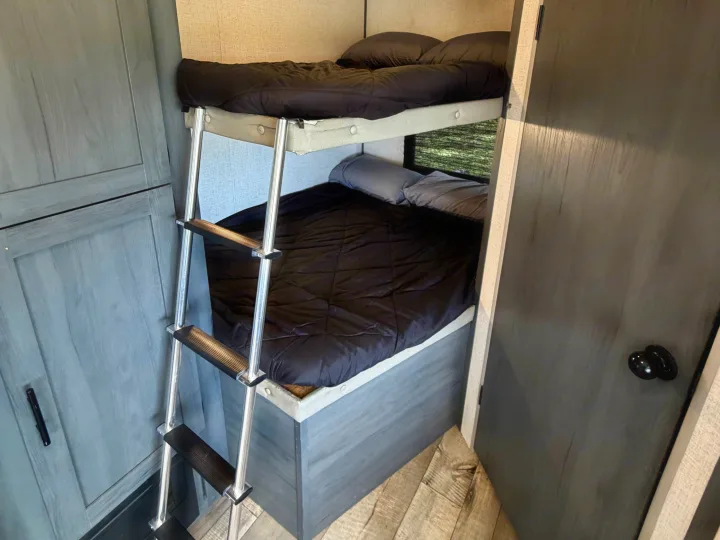 RV rental bunk beds featuring a ladder & dark bedding. A compact, cozy sleeping area inside this camper for travelers.. Dutchmen Aspen Trail LE 26BH 2022