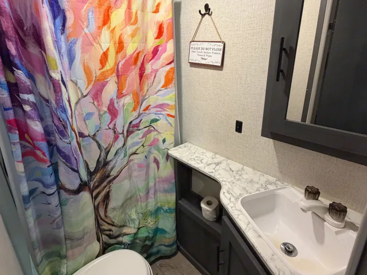 RV rental bathroom features a toilet, colorful tree shower curtain, sink, dark vanity, and a "do not flush" sign.. Dutchmen Aspen Trail LE 26BH 2022