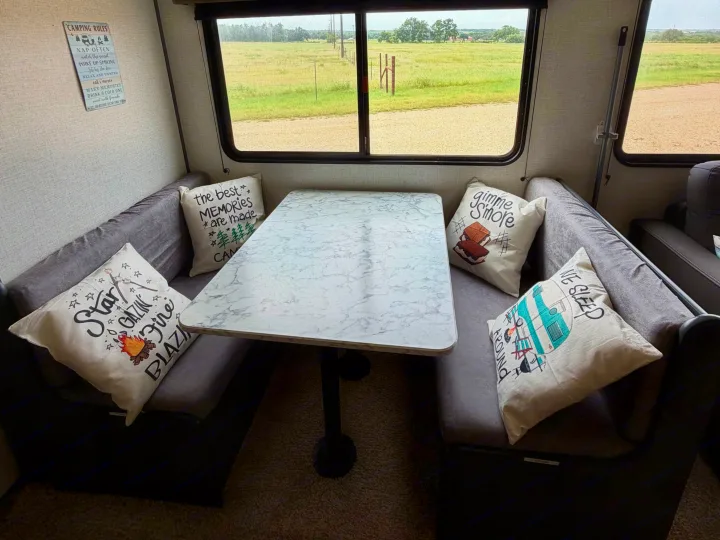 Cozy RV rental dinette with fun camping pillows, a "Camping Rules" sign, and a wide-open field view outside.. Dutchmen Aspen Trail LE 26BH 2022