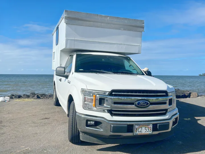 White Ford F-150 with a custom truck camper, an excellent rv rental option, parked oceanfront under blue skies.. Ford Ford F150 2019