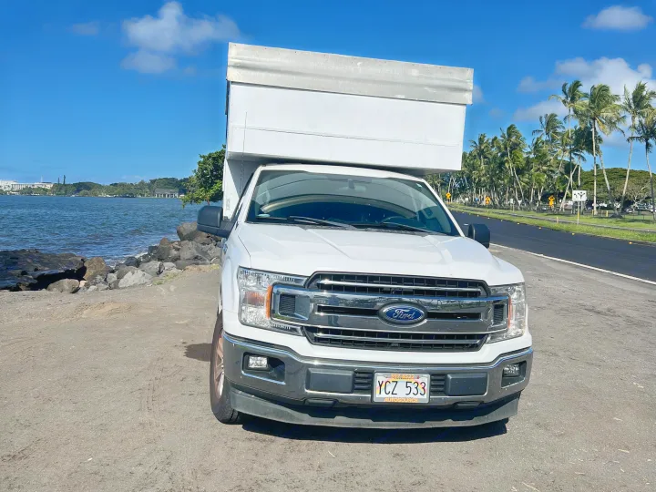 White Ford truck camper, ideal for an RV rental, parked oceanfront in Hawaii with palm trees & blue sky.. Ford Ford F150 2019