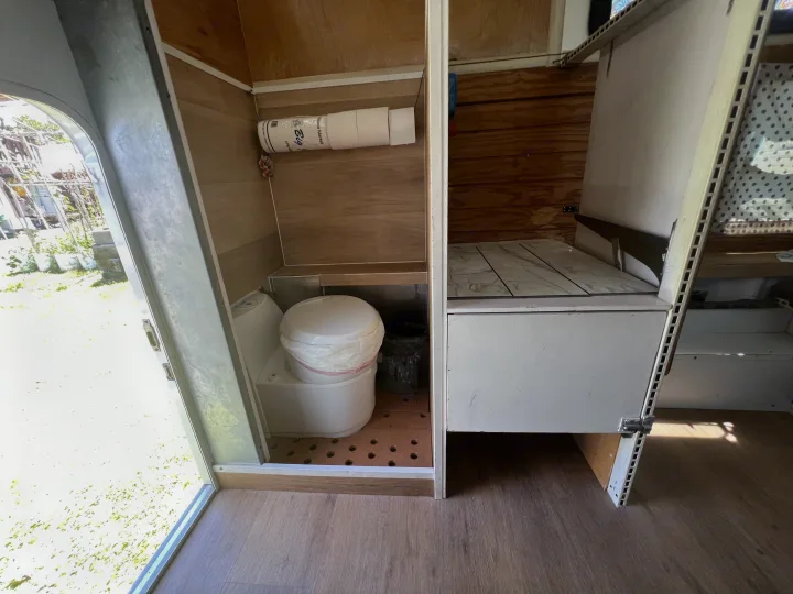 RV rental: Compact interior showing a composting toilet, toilet paper, wood walls, and open door view to outdoors.. Ford Ford F150 2019