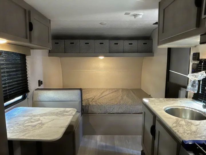 Cozy RV rental interior showcasing a bed, dinette with table, kitchen sink, and overhead storage. Ideal for travel.. Coachmen Clipper 17BH 2026