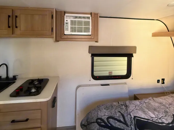 Interior of an rv rental with a kitchenette, sink, stove, wall AC, bed, and window. Ready for your road trip!. Keystone RV Coleman 2025