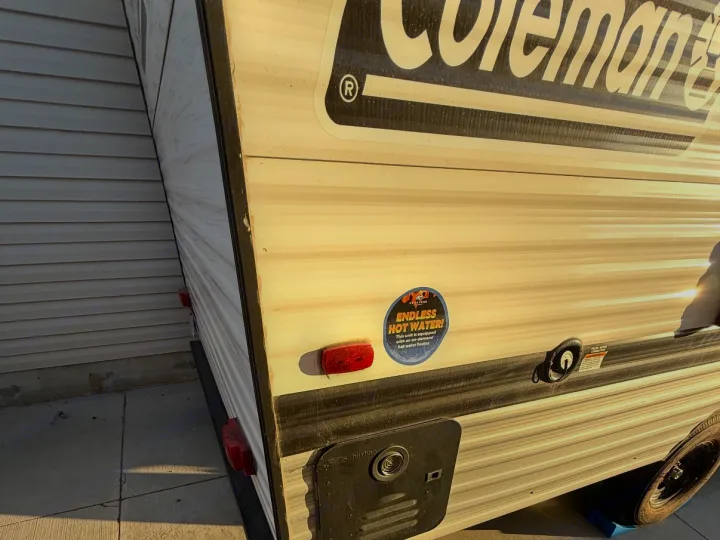 This Coleman rv rental offers endless hot water! Side view of a white and black travel trailer parked next to a house.. Keystone RV Coleman 2025