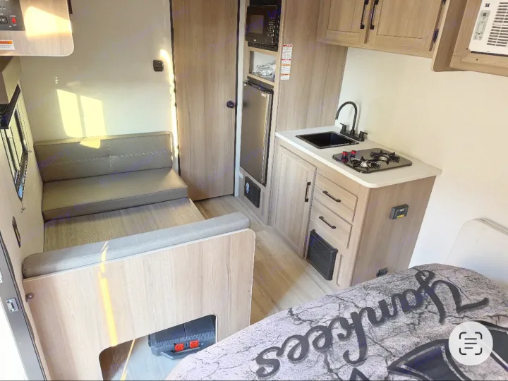 Compact RV rental interior featuring a kitchen with sink/stove, dinette, and sleeping area with a "Yankees" blanket.. Keystone RV Coleman 2025
