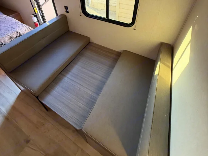 This RV rental features a bright dinette with two comfortable, cushioned benches and a wood-grain table, ideal for meals in your camper.. Keystone RV Coleman 2025