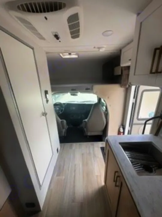 Inside this modern rv rental, the view from the rear shows a kitchenette, overhead bunk, and front cockpit area.. Thor Four Winds 2026