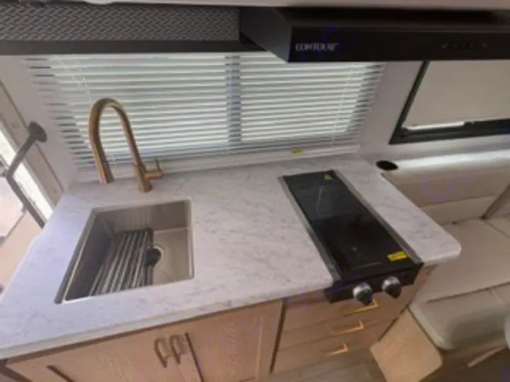 Compact RV rental kitchen features a gold faucet, stainless sink, marble-look counter, and a two-burner stovetop, perfect for travel.. Thor Four Winds 2026