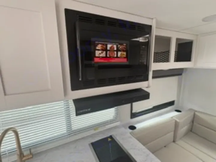 Modern RV rental kitchen with a black microwave, range hood, sink, cooktop, and bright dinette seating.. Thor Four Winds 2026