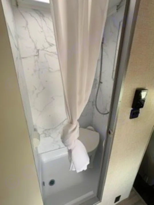 This RV rental features a compact wet bath with a shower, toilet, and modern marble-patterned walls, ideal for travel.. Thor Four Winds 2026
