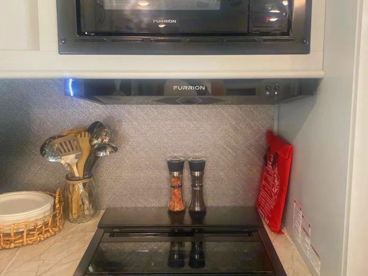 Compact rv rental kitchen with Furrion microwave, stovetop, and range hood. Utensils, salt/pepper, and fire blanket ready.. Forest River Vibe 2021