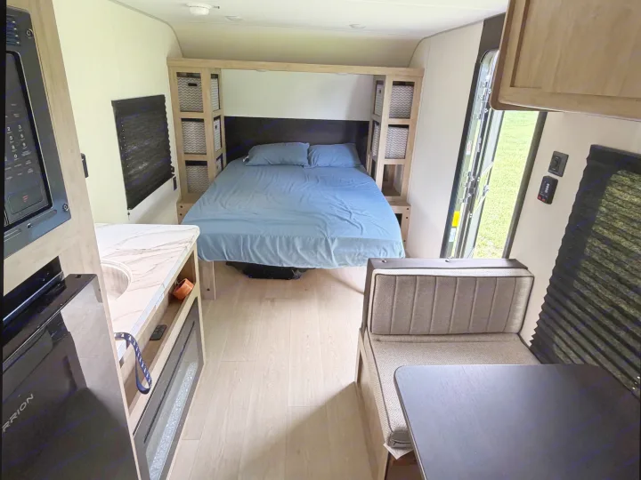 RV rental interior: cozy bedroom with blue bed, kitchen with microwave/sink, and dining booth in a compact living space.. Forest River Cherokee Wolf Pup 2026