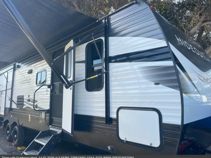 This Hideout RV rental features an extended awning, open door with steps, and a sleek black and white design.. Keystone RV Hideout 2021