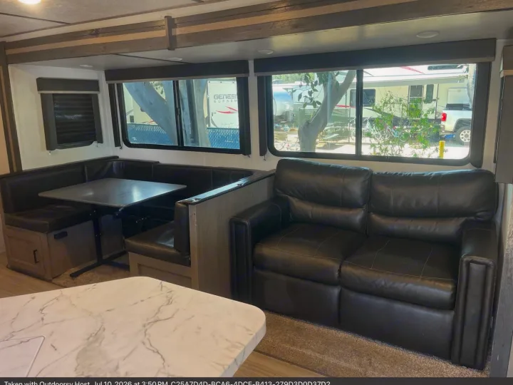Comfortable RV rental living area featuring a spacious dining booth, plush sofa, and large windows with scenic views.. Keystone RV Hideout 2021