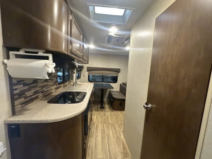 RV rental interior showcasing a compact kitchen with a sink, stovetop, and paper towel holder, next to a cozy dinette area.. Venture RV Sonic 170 VBH 2017