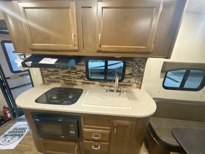 RV rental interior showcasing a cozy kitchen with wood cabinets, stove, sink, microwave, and adjacent dining booth.. Venture RV Sonic 170 VBH 2017
