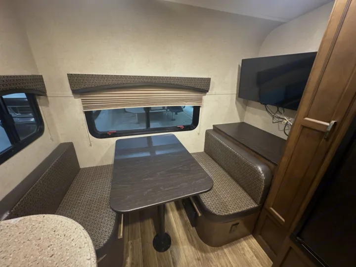 RV rental dinette features a dark wood table, patterned bench seating, wall-mounted TV, and light wood flooring.. Venture RV Sonic 170 VBH 2017