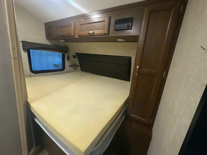 RV rental bedroom setup with a large bed, brown wooden cabinets, entertainment system, and window, perfect for your next trip.. Venture RV Sonic 170 VBH 2017