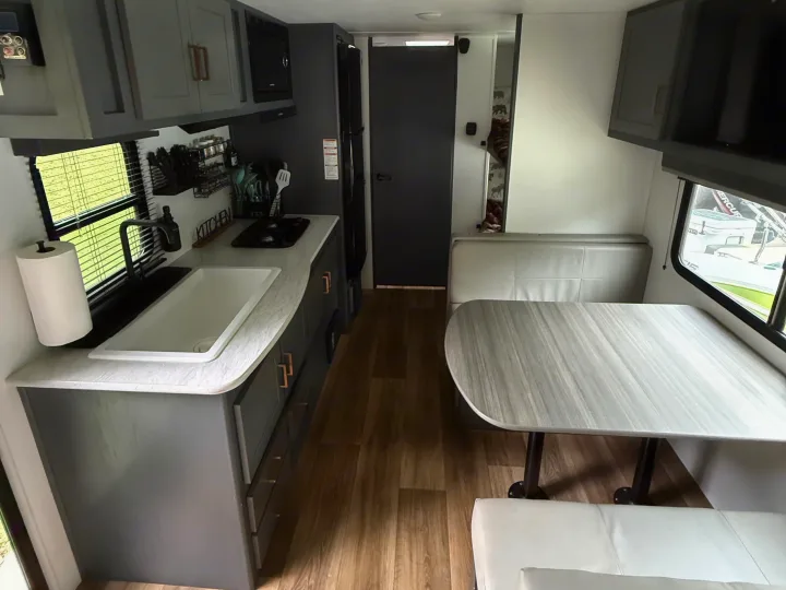 Inside an RV rental: a neat kitchen with grey cabinets, sink, dining table, and cozy booth seating, ideal for travelers.. Keystone RV Bullet Crossfire 2024