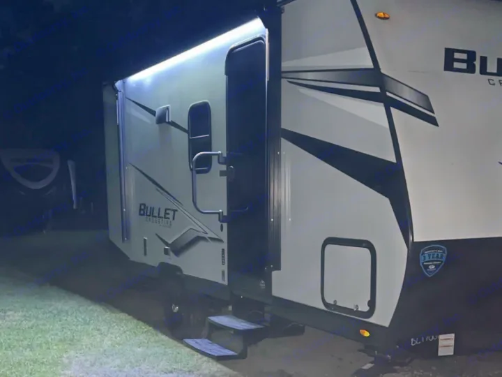 Night view of a brightly lit Bullet Crossfire RV rental at Charleston KOA. Awning lights illuminate the steps and ground.. Keystone RV Bullet Crossfire 2024