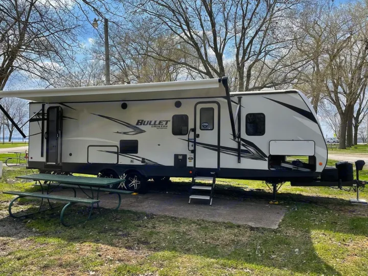 White Bullet Ultra Lite **RV rental** with extended awning at a scenic lakeside campsite, featuring a green picnic table.. Keystone RV Bullet Ultra Lite 2022