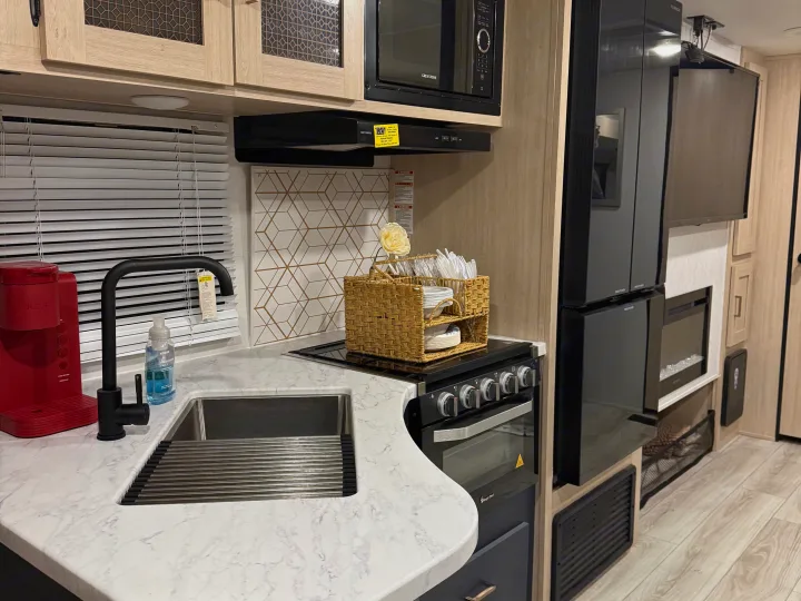 Modern RV rental kitchen boasts a marble-look countertop, Keurig, stove, microwave, and fridge, plus a cozy TV/fireplace area.. Avenger Avenger Trailer 2025