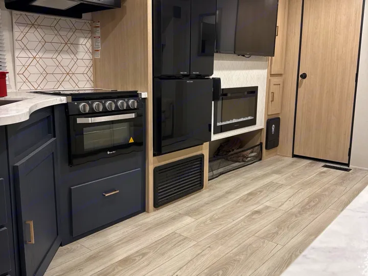 Explore this modern RV rental's kitchen, featuring a compact stove, oven, fridge, and cozy fireplace for comfort.. Avenger Avenger Trailer 2025
