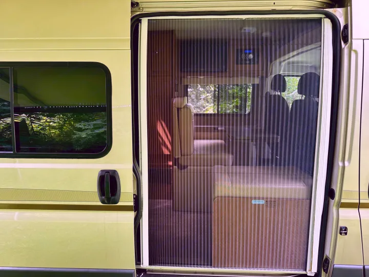 Light green RV rental: side door open with pleated screen, revealing interior seating & controls of the campervan.. Winnebago Travato 2014
