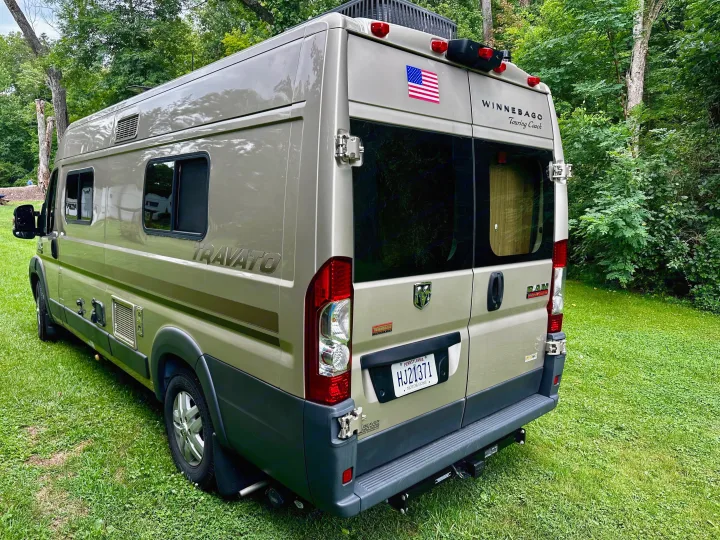 Olive green Winnebago Travato camper van, ideal for an rv rental adventure, parked on grass in a wooded setting.. Winnebago Travato 2014