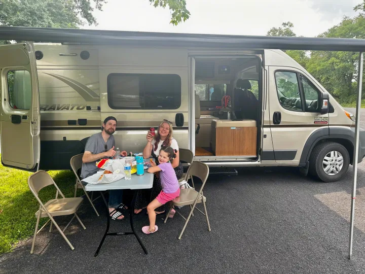 Family enjoying a meal outside their RV rental van. Ideal for a camping trip or family road trip adventure.. Winnebago Travato 2014