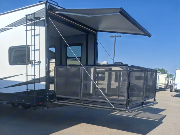 This white RV rental features an extended rear patio deck with railings and an overhead awning, ready for outdoor enjoyment.. Grand Design Momentum Toy Hauler 2022