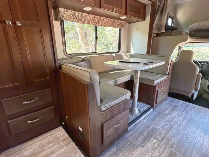 Inside an rv rental: a cozy dinette with U-shaped seating, table, wood cabinets, and large window; front cab & overhead bunk visible.. Forest River Forester Classic 2291S 2020