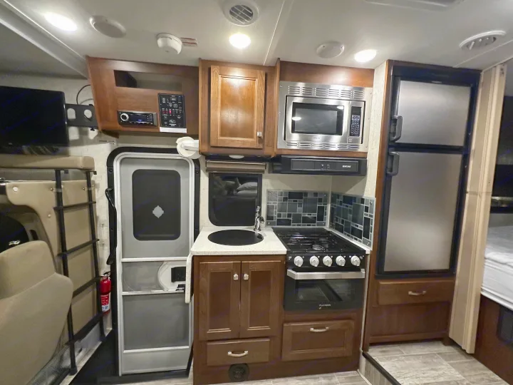 Inside an RV rental: full kitchenette (microwave, oven, fridge), main controls, bunk bed, & entrance.. Forest River Forester Classic 2291S 2020